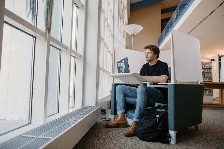 在电子游艺信誉排行的图书馆里，一名男生拿着笔记本电脑坐在椅子上望着窗外